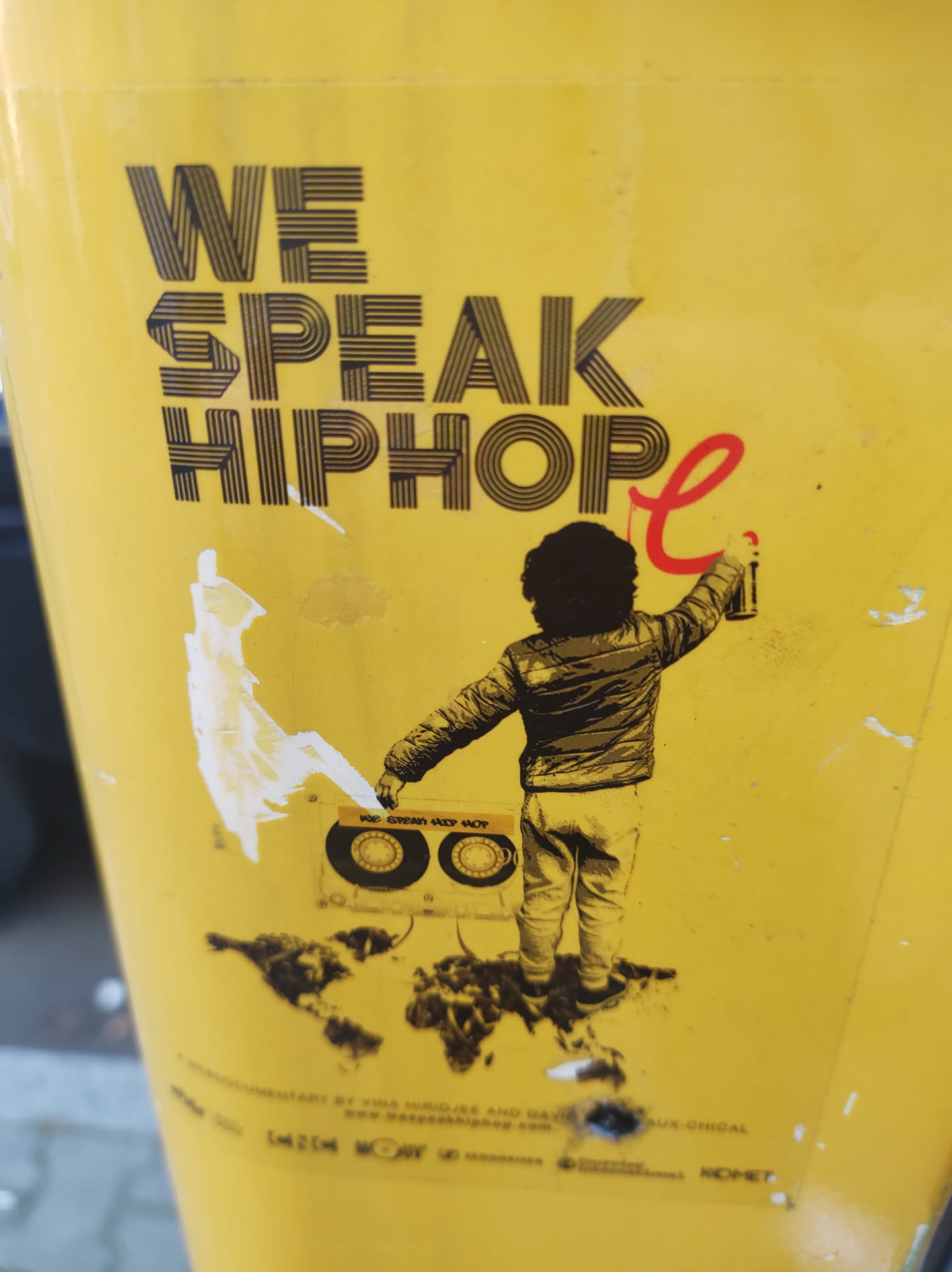 A yellow sticker featuring a stylized image of a person holding a boombox and spray painting. The text 'WE SPEAK HIPHOP' is prominently displayed.  The design suggests a connection to hip-hop culture.