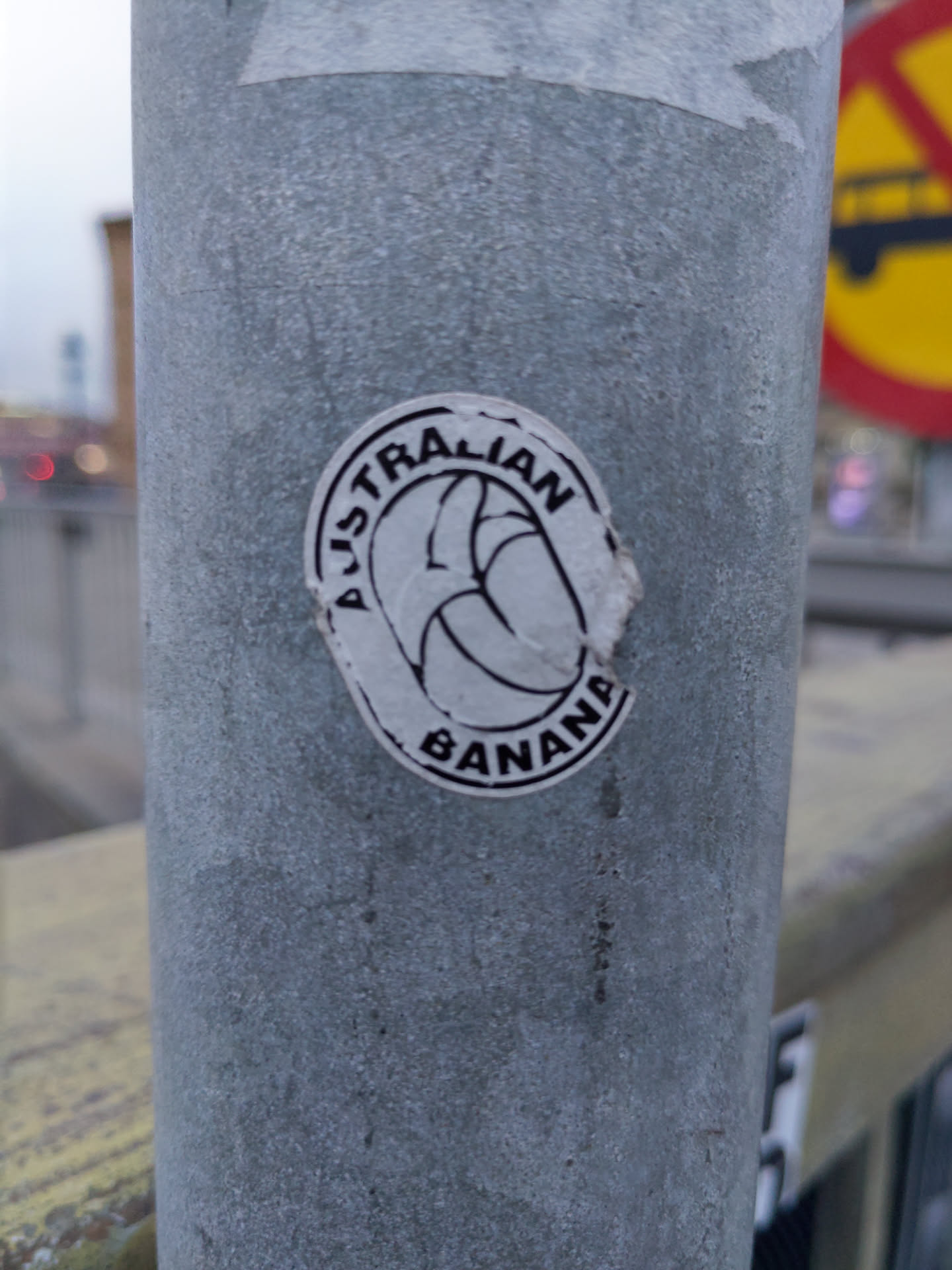 A round sticker featuring a stylized banana with the text "Australian Banana" encircling it.  The sticker is affixed to a metal pole.