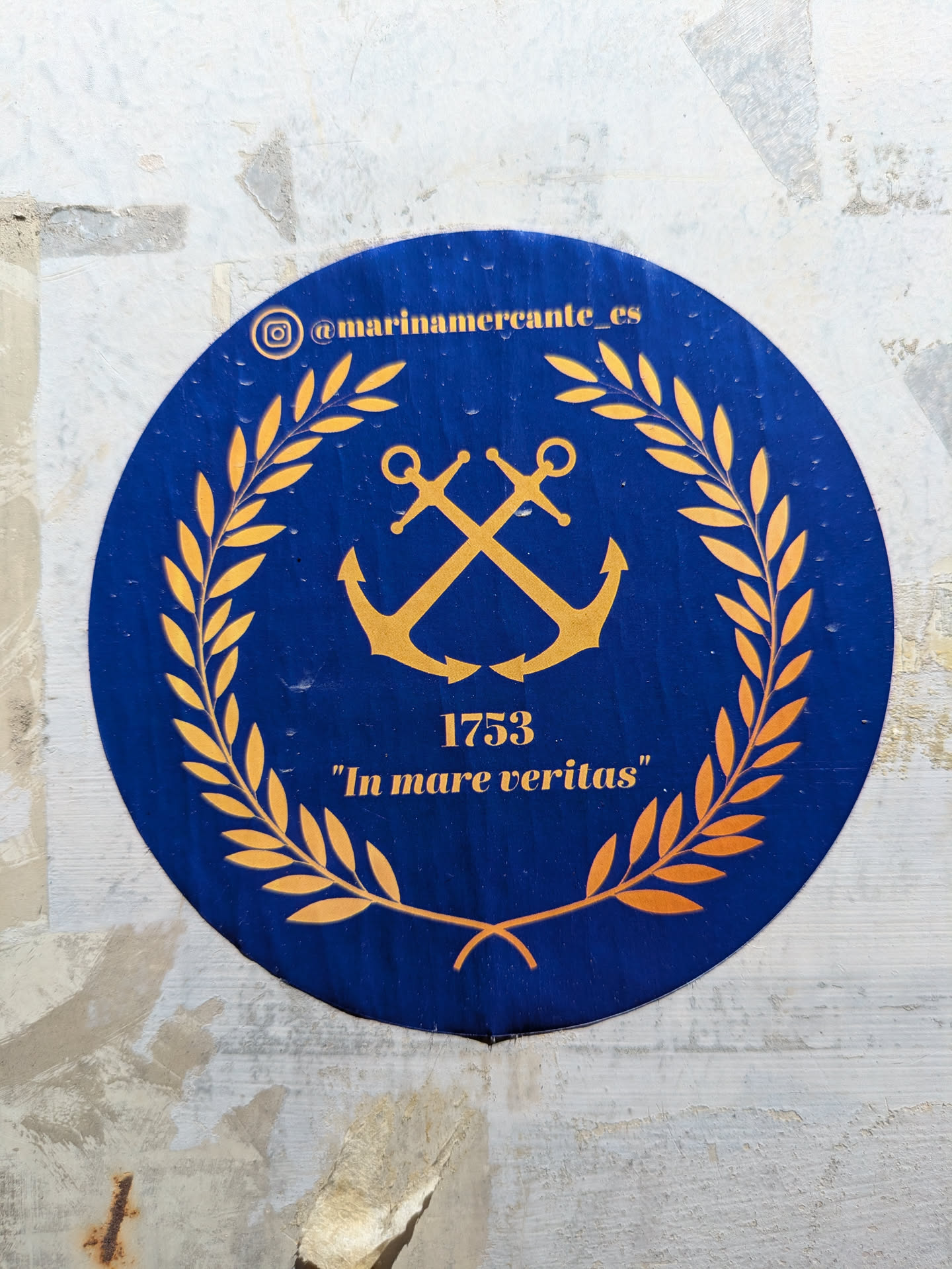 The sticker is a round, blue background with gold-colored elements. At the center, there is a crossed anchors emblem surrounded by a laurel wreath. Above the emblem and along the edge of the sticker is the Instagram handle "@marinamercante_es". Below the emblem, the number 1753 is displayed, followed by the text "In mare veritas" in quotation marks.