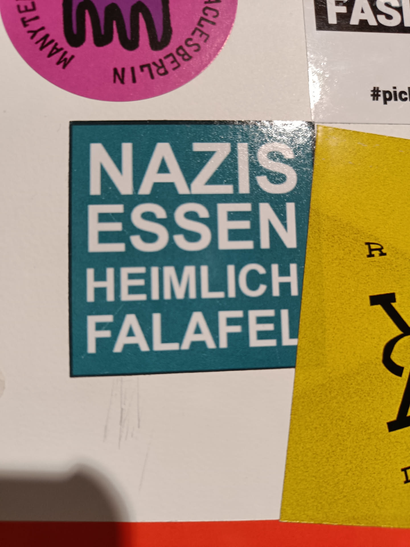A teal square sticker with white text that says Nazis Essen Heimlich Falafel.  It's a humorous statement suggesting a surprising food preference.