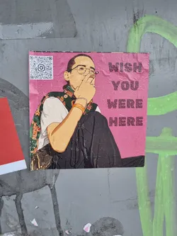 A sticker featuring an illustration of a person smoking a cigarette with the text 'Wish You Were Here'.  The sticker has a pink background and includes a QR code linking to Instagram.