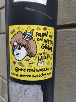 Yellow sticker with a drawing of a person with a big furry hat and sunglasses, and a cat on top of the hat. There are also other small drawings around and social media information at the bottom. 