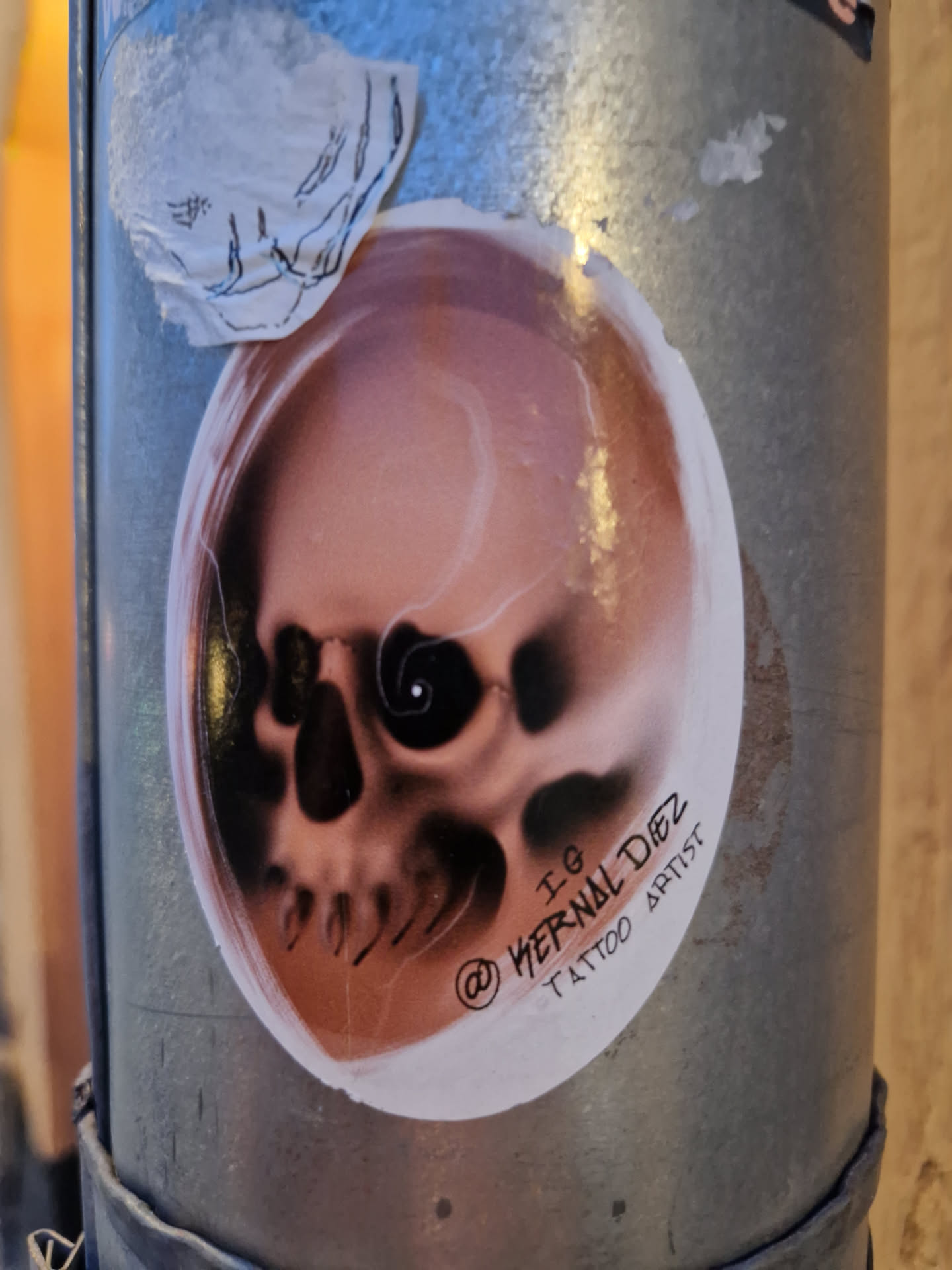 A sticker featuring a detailed illustration of a skull, created by tattoo artist @wernaldiez. The sticker is oval-shaped and features a pinkish-brown skull with shading and detail. The artist's Instagram handle is visible on the sticker.