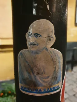 A slightly worn sticker featuring an image of Mahatma Gandhi.  The sticker has text at the bottom that reads 'Mahatma Gandhi'.