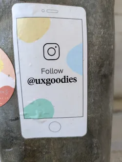 A sticker shaped like a white smartphone with a screen displaying the Instagram logo and the text 'Follow @uxgoodies'. The background has abstract shapes in yellow, blue, and green.