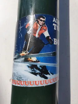 A weathered sticker featuring a skier in retro gear. The text partially visible says 'Always Time to Bomb'. The bottom features a repeating 'u'