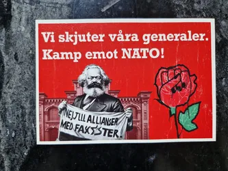 A sticker featuring Karl Marx holding a banner that says "Nej till allianser med fascister."  There's also a red rose with a fist in the middle, symbolizing resistance. The text on the sticker translates to "We shoot our generals. Fight against NATO!"