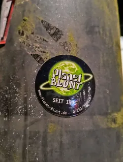 A worn Planet Blunt sticker on a dark surface.  The sticker features the company's logo and website address.