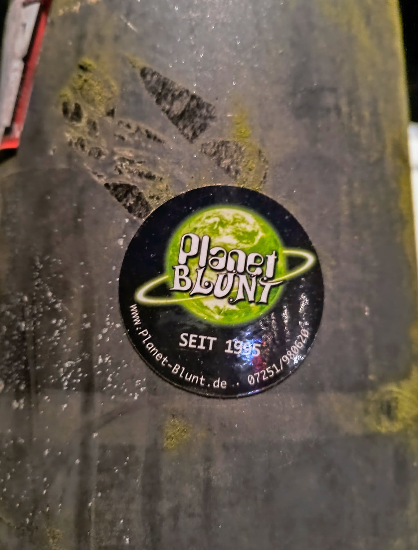 A worn Planet Blunt sticker on a dark surface.  The sticker features the company's logo and website address.