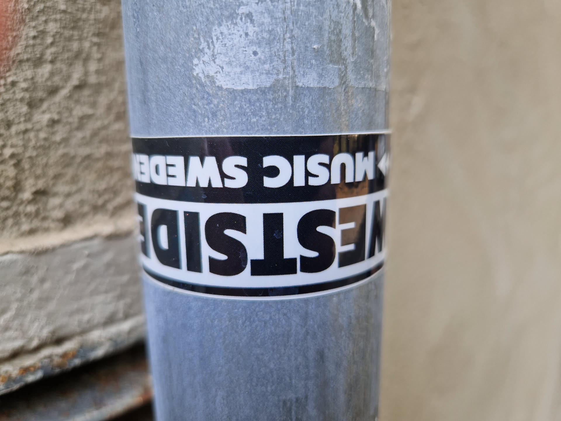 Close-up of a black and white sticker on a metal pipe. The sticker says "Westside Music Sweden" with the words arranged in a unique way.