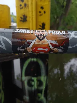 A sticker featuring a man with a beard, glasses, and a Superman logo on his chest.  The text above his head reads "SANKT PAULI!"