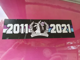 A black sticker commemorating the years 2011 and 2021, featuring a stylized image of a figure with crossed weapons and a laurel wreath, along with the text "Djurgården Osnabrück".