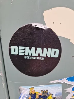 Round black sticker with the word DEMAND written in a teal sans-serif font. Below the text is the instagram handle @DEMANDSTHLM.