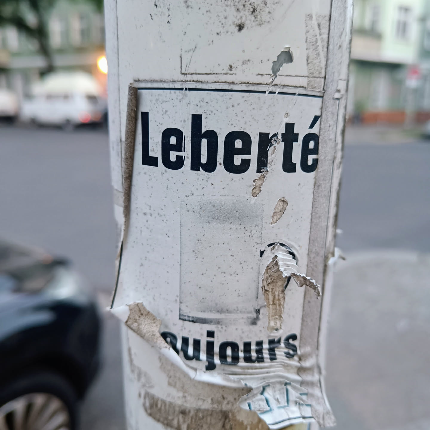 A torn and weathered street poster featuring the French words "Liberté toujours", which translates to "Liberty always".  The poster shows significant signs of wear and tear, suggesting it has been exposed to the elements for a considerable time.