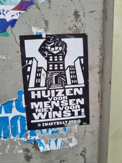 A sticker depicting a fist emerging from a building, with the text "HUIZEN VOOR MENSEN NIET VOOR WINST!" (Houses for people, not for profit!).  The sticker also includes a website address.