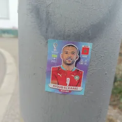 A sticker featuring Ayoub El Kaabi, a Moroccan footballer. The sticker includes his name, birthdate (25-6-1993), height (1.82 m), and the year 2018, possibly referencing a FIFA World Cup appearance.  The Moroccan flag is also displayed. The sticker has a player card design.