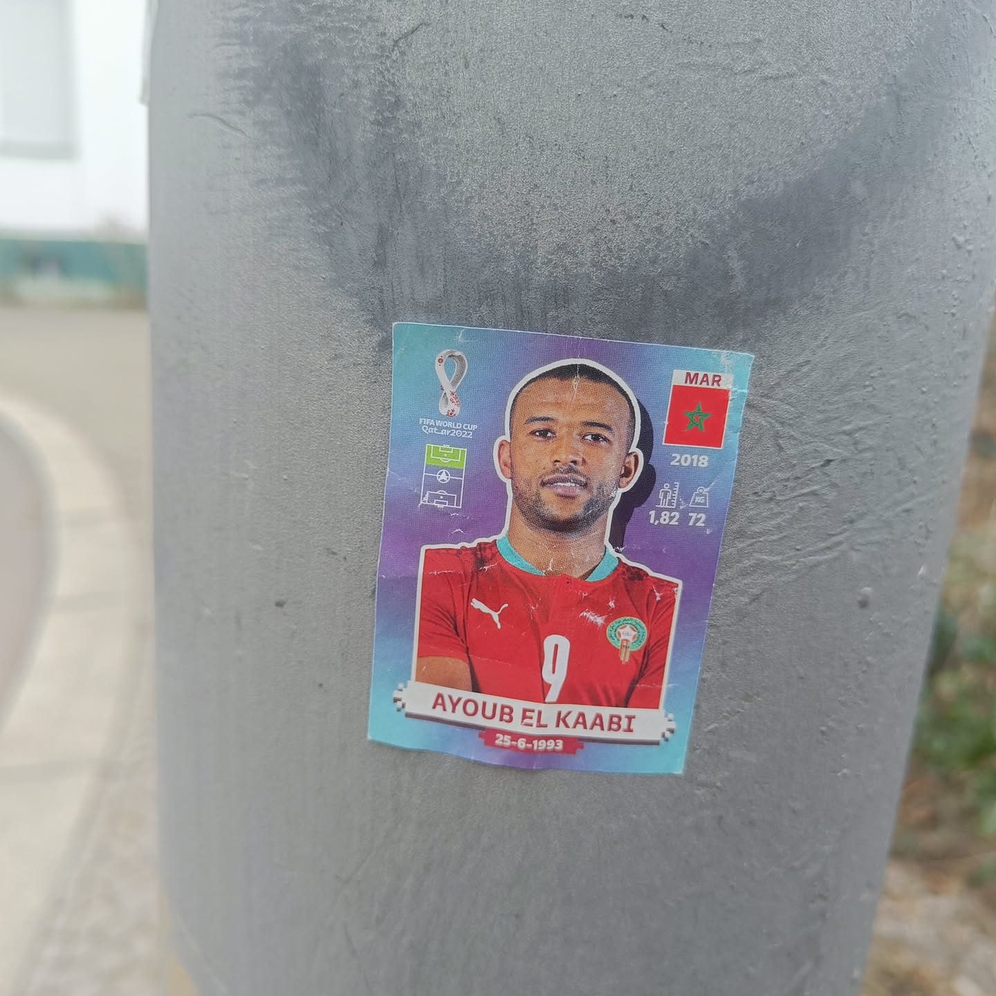 A sticker featuring Ayoub El Kaabi, a Moroccan footballer. The sticker includes his name, birthdate (25-6-1993), height (1.82 m), and the year 2018, possibly referencing a FIFA World Cup appearance.  The Moroccan flag is also displayed. The sticker has a player card design.