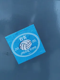 A blue square sticker with a white circular logo. The logo features the initials "BK" above a volleyball graphic, with the text ".20 ARSLERUD 19." arranged around it.  The sticker appears to be for a volleyball club.