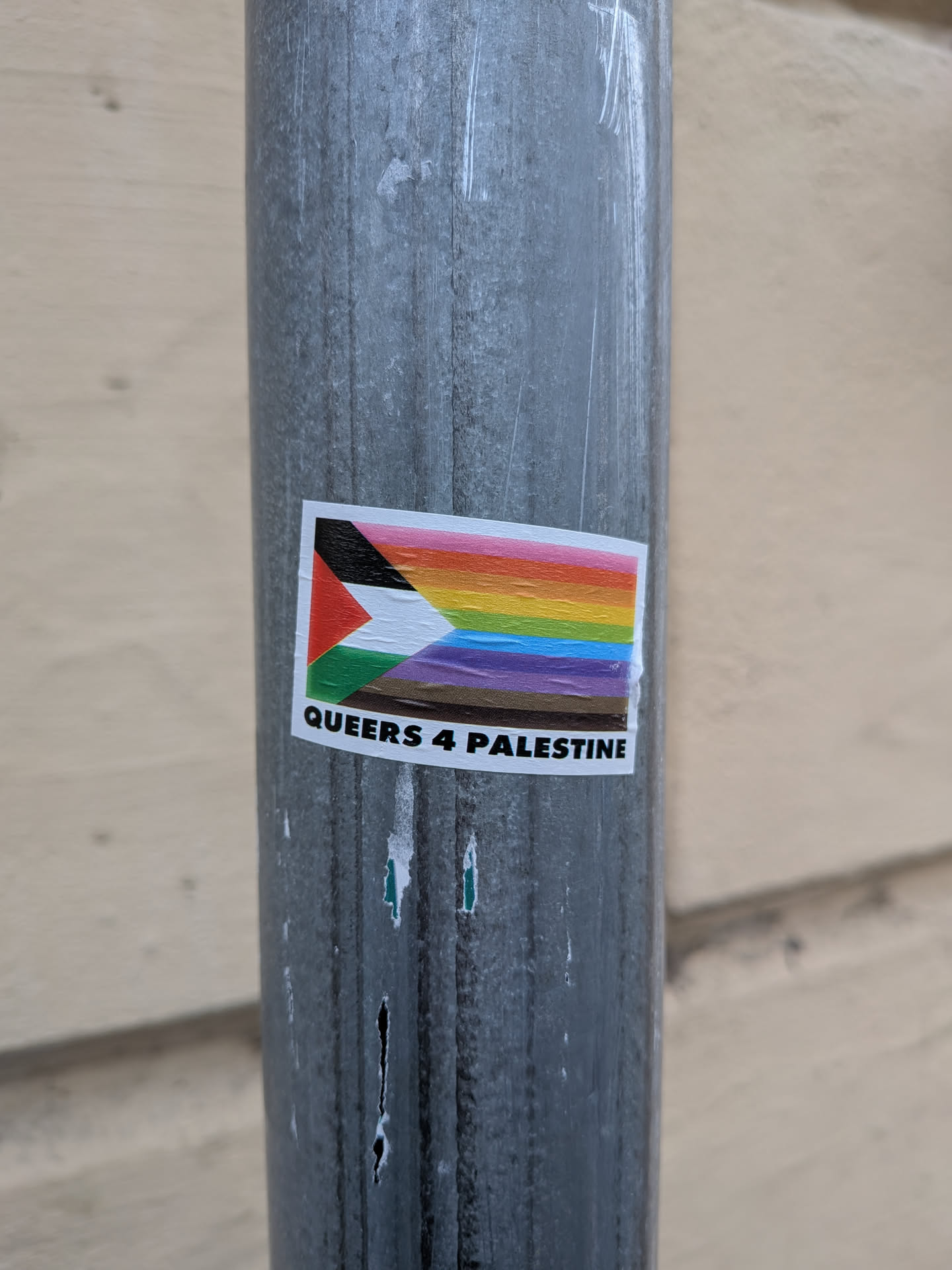 The sticker features a composite flag design. The left side incorporates the black, white, red, and green triangles of the Palestinian flag. To the right of this, a rainbow gradient is depicted, transitioning through pink, orange, yellow, green, blue, and purple, representing the LGBTQ+ pride flag. Below the flag imagery, the text 'QUEERS 4 PALESTINE' is printed in bold white capital letters on a black background.