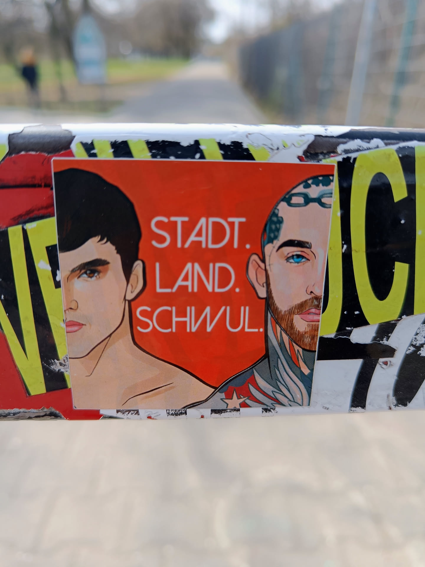 A sticker featuring an illustration of two men, with the text "Stadt. Land. Schwul." which translates to "City. Country. Gay." in German. The sticker has a bold red background with the text in white. The illustration style is clean and modern, the men appear to be stylized portraits.