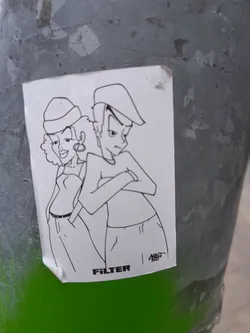 A white sticker with a black line drawing of a cool couple with the word "FILTER" at the bottom left. The drawing has a distinctive, retro style, with the woman in a strapless top and a hat, and the man with crossed arms and a similar hat.