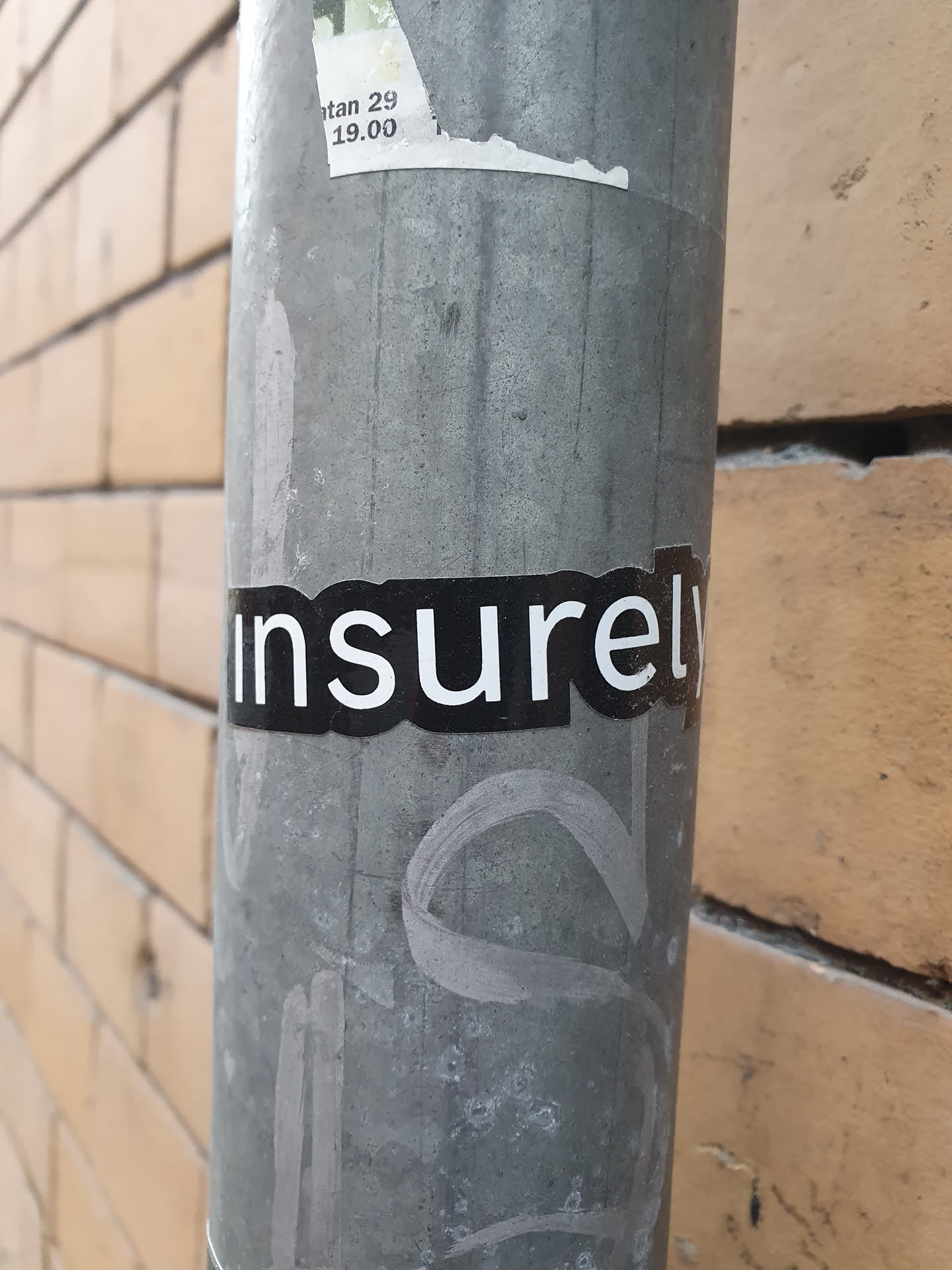 A black and white sticker with the word "insurely" on a grey metal pole. The sticker is slightly worn and there are other markings on the pole.
