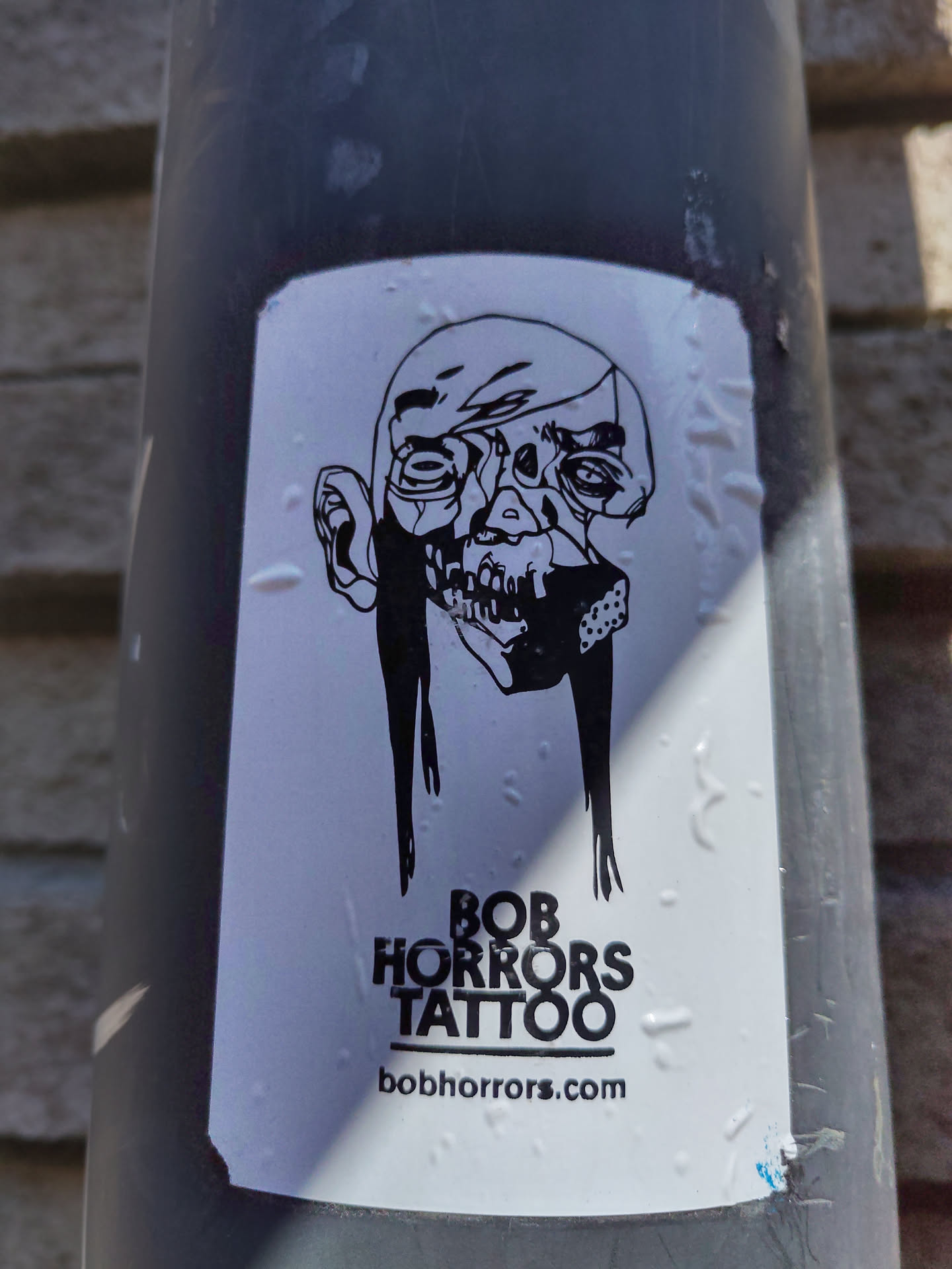A black and white sticker featuring a skull-like face with long hair, and the text "BOB HORRORS TATTOO" and website address bobhorrors.com.