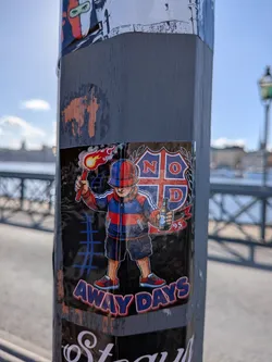 Street sticker A rectangular sticker depicting an illustrated football fan wearing a red and blue bucket hat, tracksuit top, and shorts. The character holds a smoking, burning flare aloft in one hand and a beer bottle in the other. Behind him is a crest divided by a cross featuring the letters 'N', 'O', 'D' and the number '95'. At the bottom, the words 'AWAY DAYS' are printed in bold blue letters outlined in red.