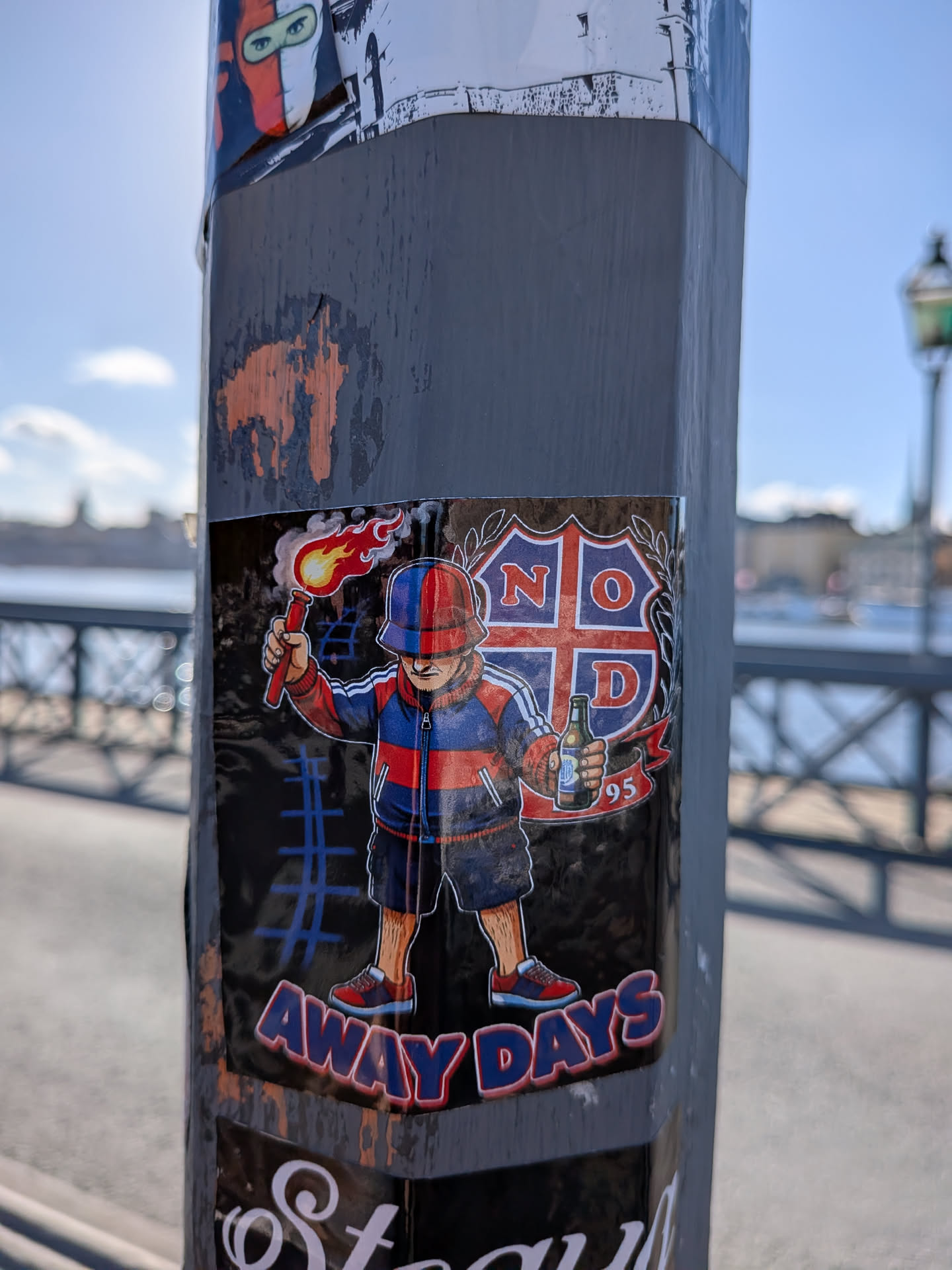 A rectangular sticker depicting an illustrated football fan wearing a red and blue bucket hat, tracksuit top, and shorts. The character holds a smoking, burning flare aloft in one hand and a beer bottle in the other. Behind him is a crest divided by a cross featuring the letters 'N', 'O', 'D' and the number '95'. At the bottom, the words 'AWAY DAYS' are printed in bold blue letters outlined in red.