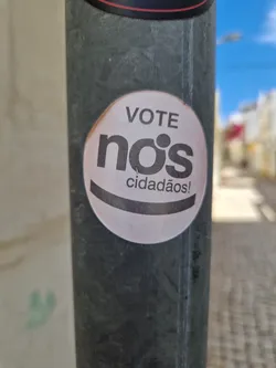 A round sticker on a pole with the text "VOTE nós cidadãos!" in Portuguese, which translates to "Vote us citizens!"