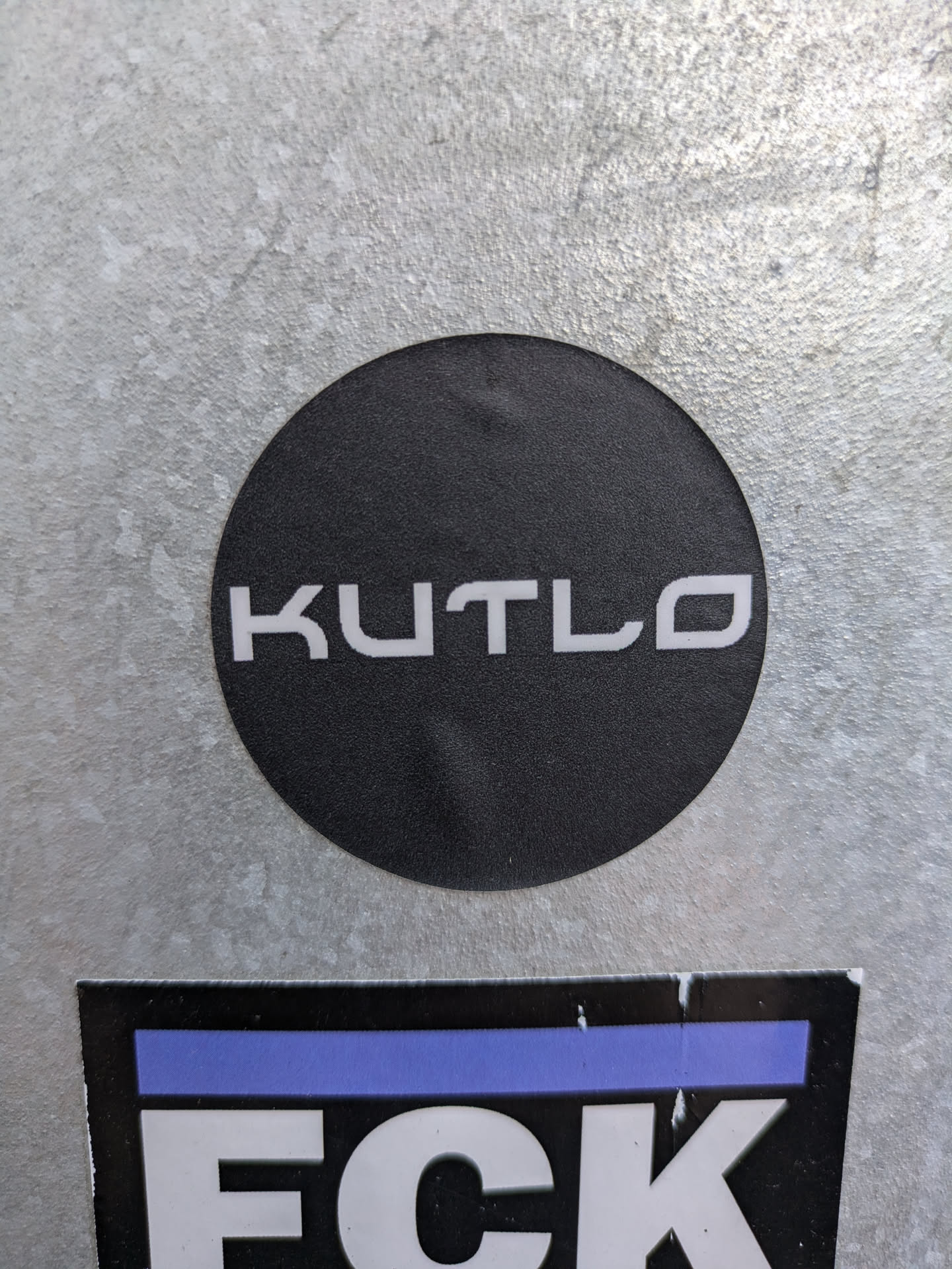 A round black sticker with the word KUTLO in white sans-serif uppercase letters. 