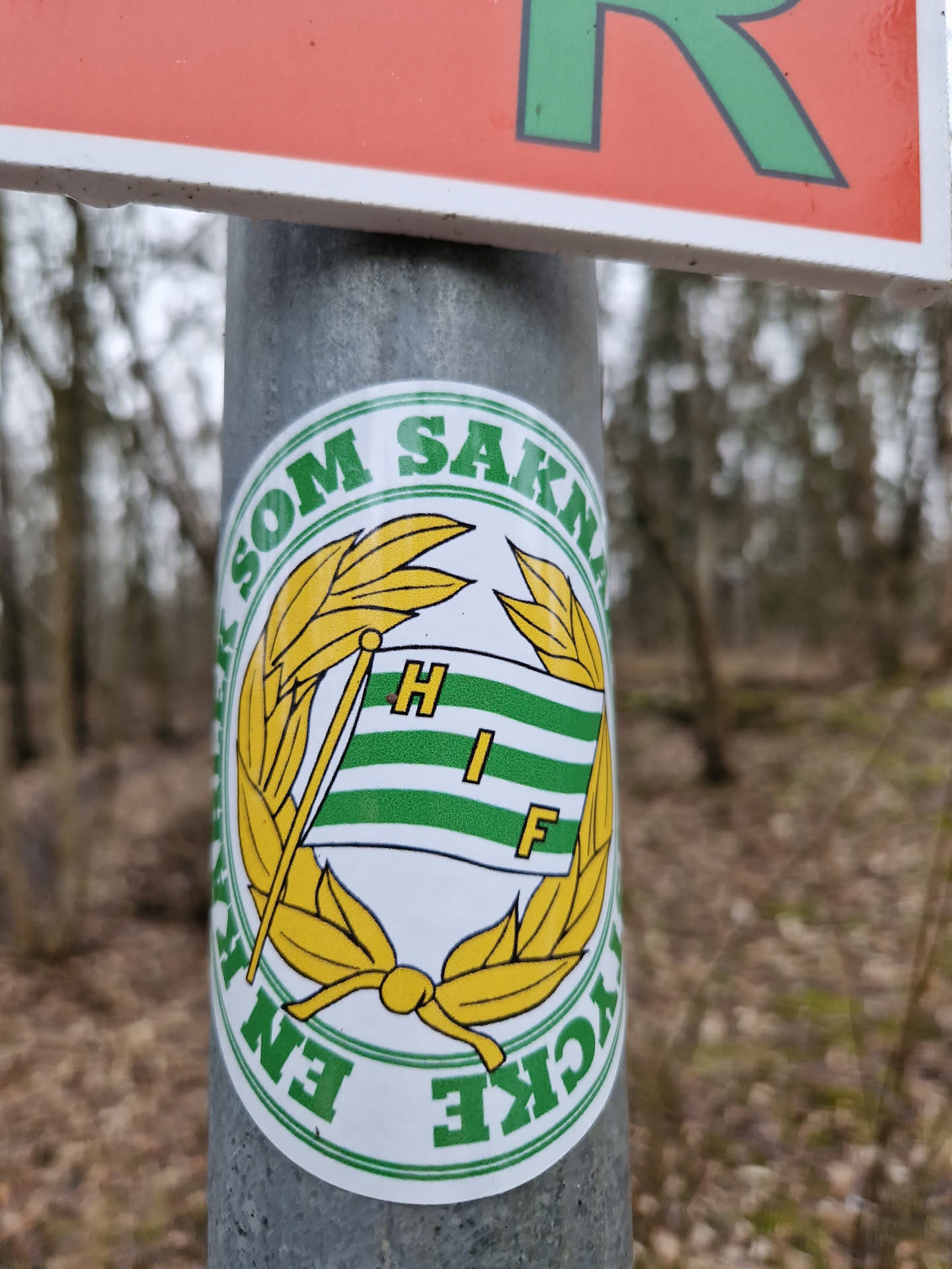 A round sticker featuring a flag with the letters HIF in the middle of a laurel wreath. The text around the emblem says "En som saknar HIF", which translates to "One who misses HIF".