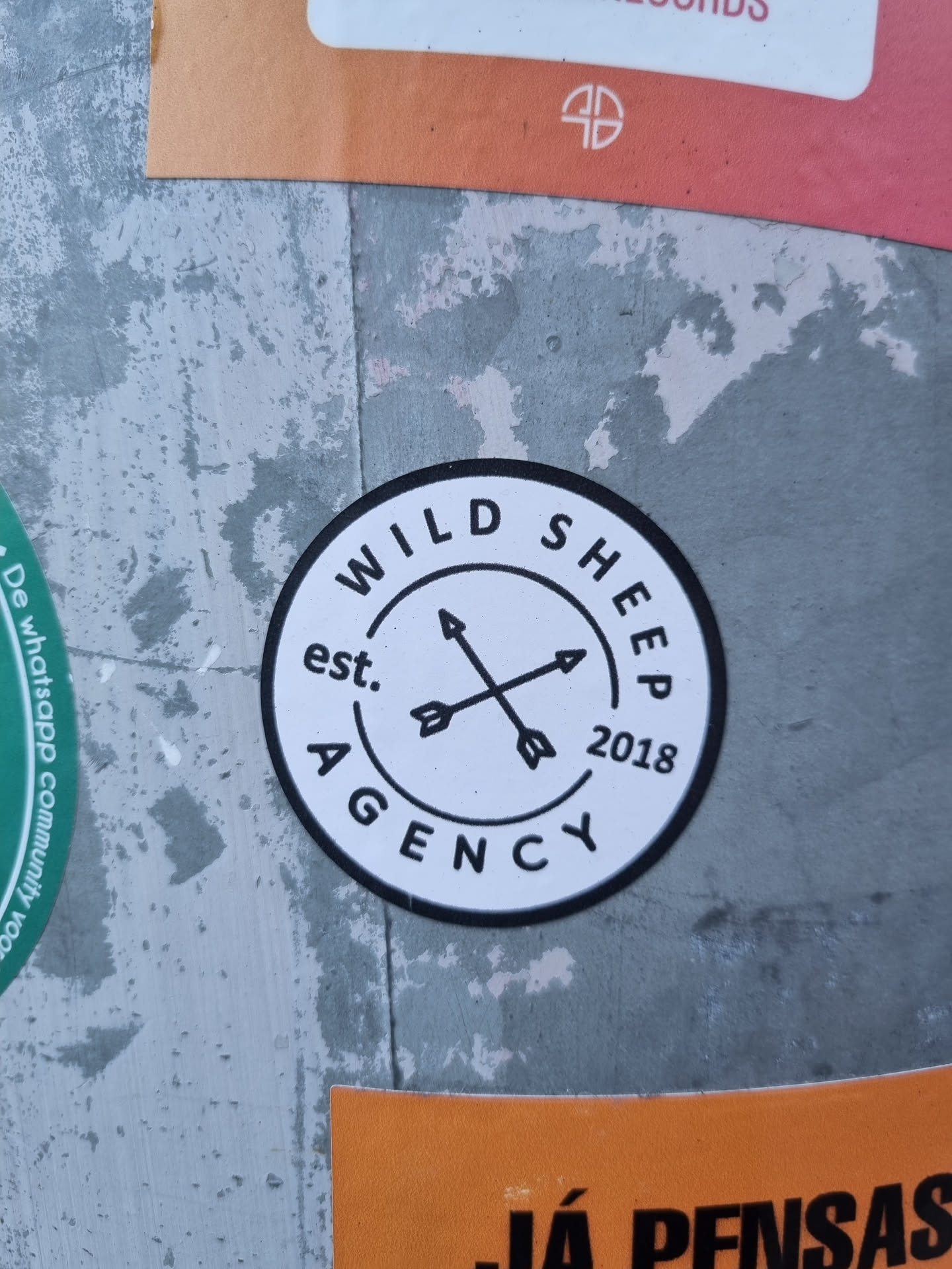 Round sticker with black and white design. It has the text "Wild Sheep Agency" written in a circle, with the years "est. 2018" written on the bottom. In the center there are two crossed arrows. 