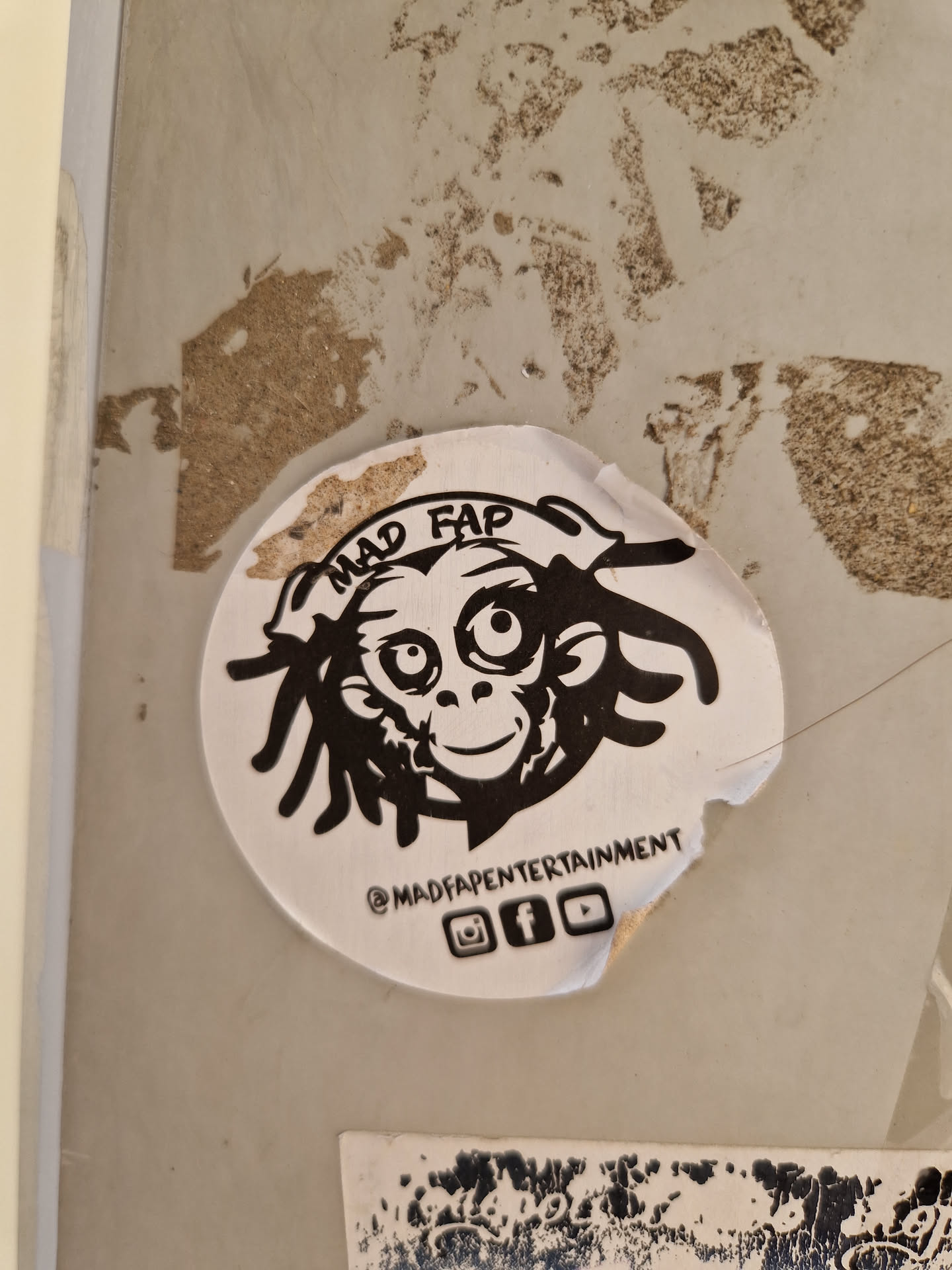 A round sticker with a black and white illustration of a monkey with dreadlocks. The text "MAD FAP" is written above the monkey, and "@MADFAPENTERTAINMENT" is written below. Social media icons for Instagram, Facebook, and YouTube are also included.