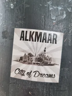 Street sticker A vintage-style sticker depicting Alkmaar, Netherlands. The sticker features a sepia-toned image of the city's iconic waterfront and buildings, with the city's name prominently displayed.  The tagline 'City of Dreams' adds a whimsical touch.