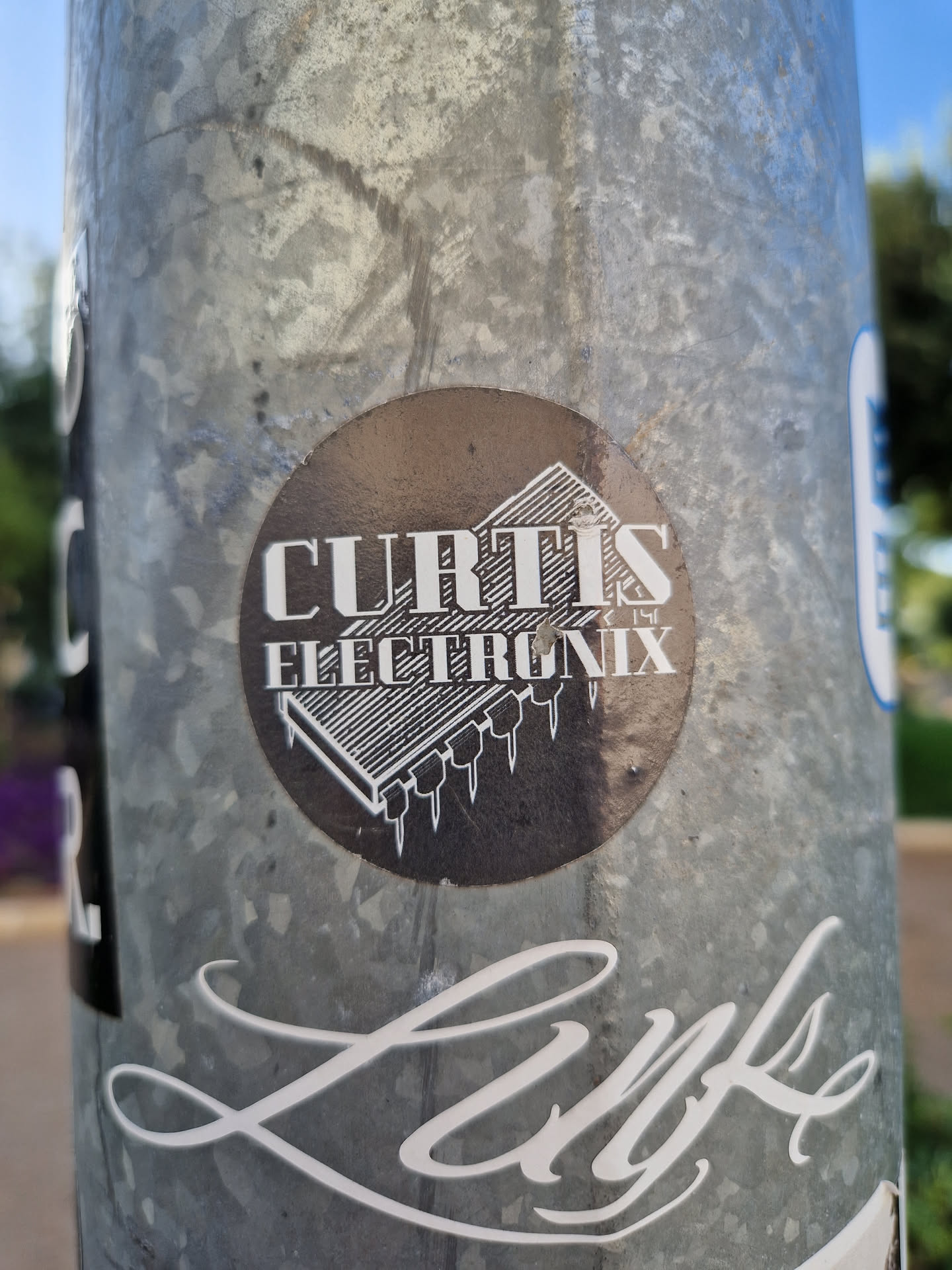 A round sticker with the text 'Curtis Electronix' and an image of an integrated circuit. The sticker is affixed to a metal pole.