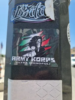 A sticker featuring a stylized illustration of a man with a gun, set against a camouflage background with Italian flag colors. The text "Army Korps Ultra Monopoli" is prominently displayed.