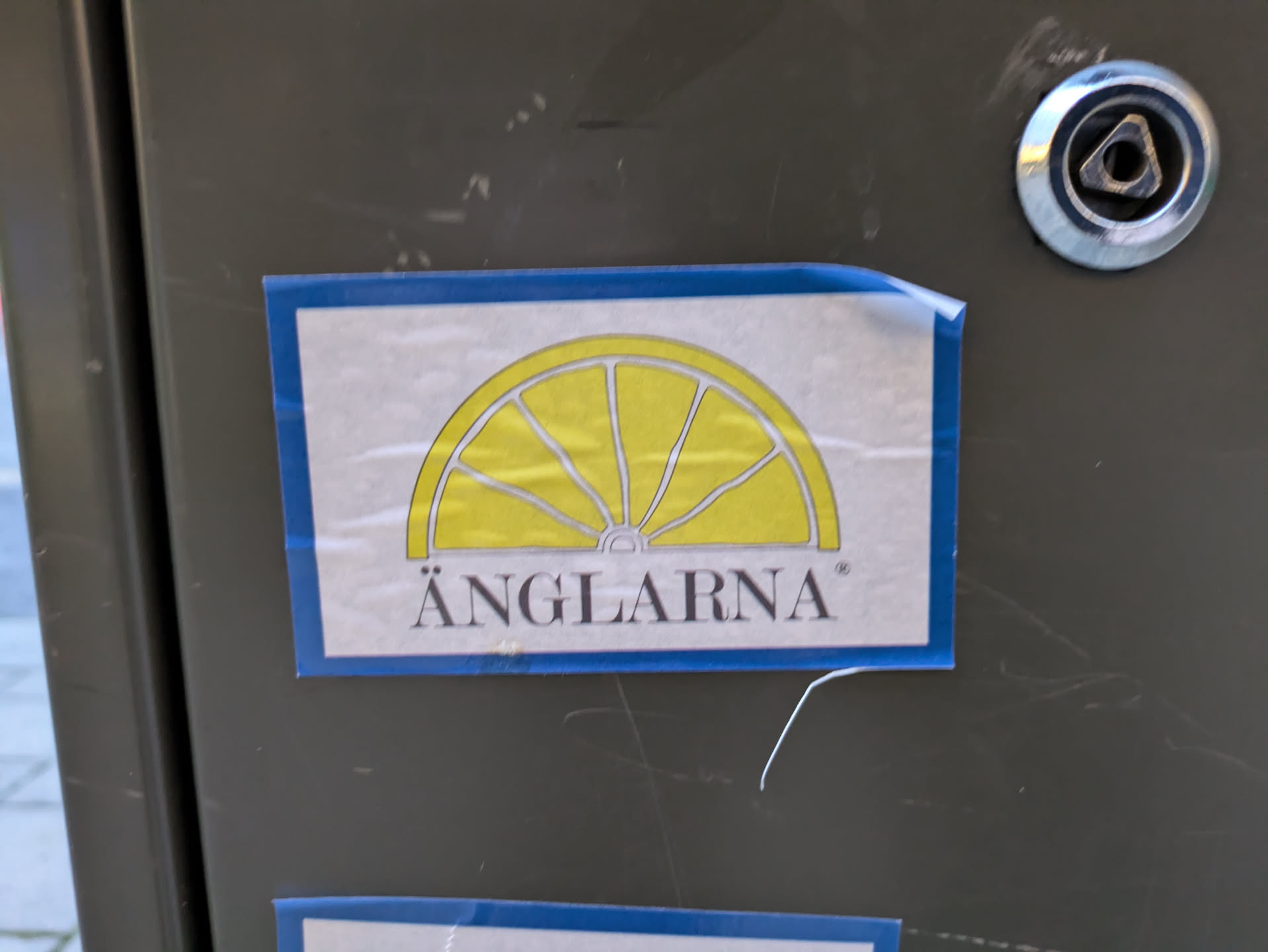 A sticker featuring a yellow lemon slice graphic and the text ÄNGLARNA. The sticker has a simple design with a blue border.