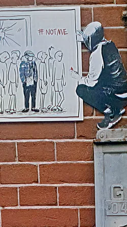 The sticker portrays a poignant scene: a row of similar-looking figures, with one figure standing out in a distinct outfit. They stand before a window that appears to be shattered, hinting at exclusion or escape. The graffiti-like tag '#NOTME' underscores the theme of individuality or dissent. Beside it, there is another sticker of a person painting the wall. The artwork is placed against a textured brick wall, adding an urban feel.