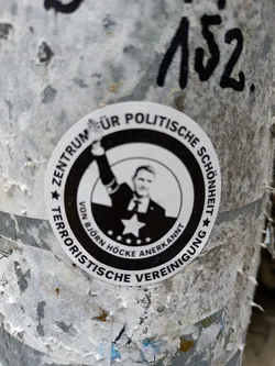 A worn-out sticker featuring a black and white image of Björn Höcke with text suggesting a center for political beauty, recognized by Björn Höcke, and labeled a terrorist organization.
