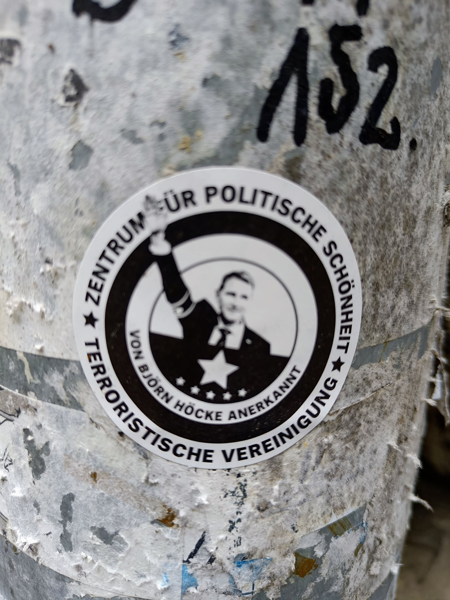 A worn-out sticker featuring a black and white image of Björn Höcke with text suggesting a center for political beauty, recognized by Björn Höcke, and labeled a terrorist organization.