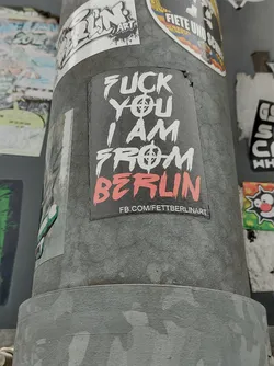 A sticker with a bold statement: "Fuck you I am from Berlin." It features a graphic design with a symbol that seems to be a stylized anarchy symbol. The sticker also has a Facebook link at the bottom.