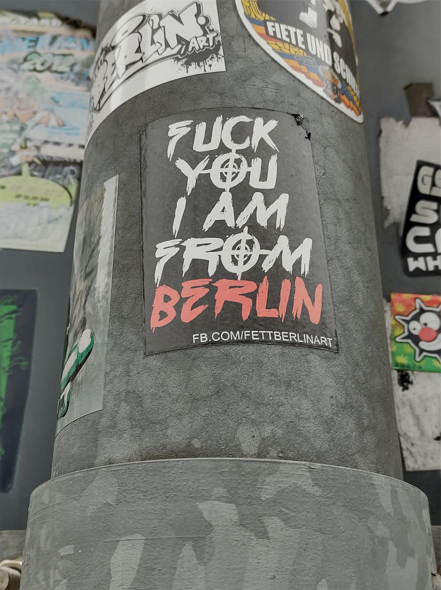 A sticker with a bold statement: "Fuck you I am from Berlin." It features a graphic design with a symbol that seems to be a stylized anarchy symbol. The sticker also has a Facebook link at the bottom.