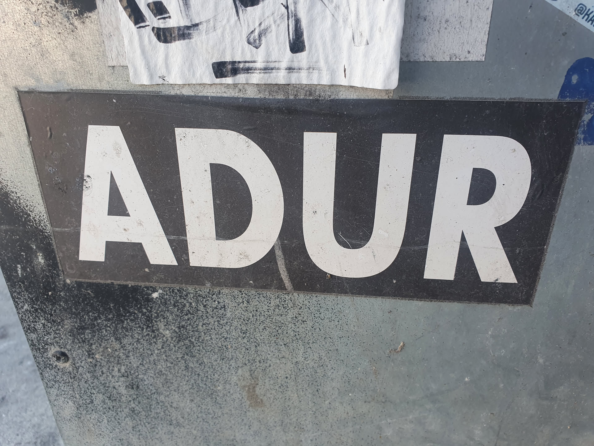 A black sticker with white capital letters spelling ADUR. The sticker is slightly dirty and weathered.