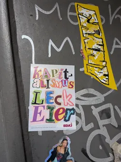 Street sticker A vertically oriented rectangular sticker designed in a colorful ransom-note or collage style on a lined notebook paper background. It displays the text 'KAPit-aLiSmuS LECK Eier' in mismatched, vibrant fonts and textures. In the bottom right corner is the logo 'SDAJ' accompanied by a five-pointed star, and on the bottom left is small publisher legal text reading 'ViSdP: Andrea Hornung, Hoffnungstr. 18, 45127 Essen'.
