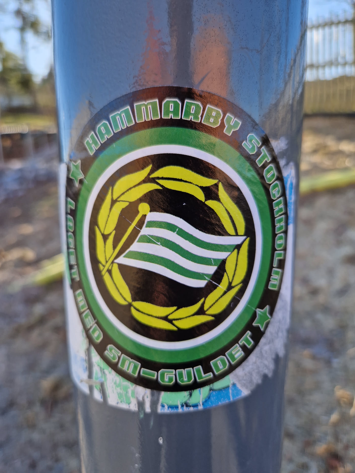 A round sticker featuring the Hammarby Stockholm logo. The logo includes a flag with green and white stripes, surrounded by a yellow wreath. The text "HAMMARBY STOCKHOLM" is written in a circular fashion around the logo, and the text "SM-GULDET" is partially visible at the bottom.