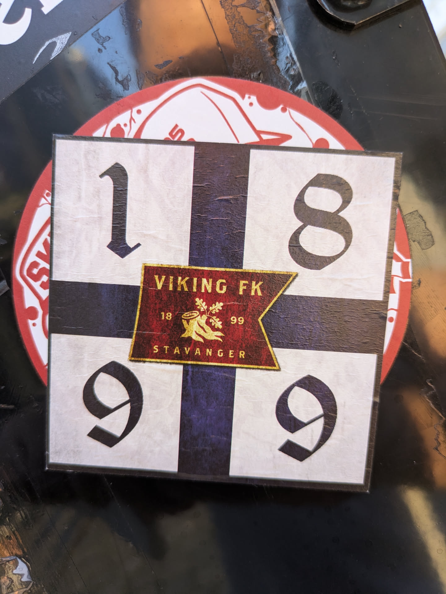 The sticker is square-shaped with a white background and a dark blue/purple Nordic cross. Large black numbers '1', '8', '9', '9' are prominently displayed in each quadrant, forming the year 1899. In the center, there is a shield-shaped emblem in red and gold. This emblem contains the text 'VIKING FK' at the top, an image of an oak tree stump with foliage in the middle, flanked by the numbers '18' and '99'. At the bottom of the emblem, the word 'STAVANGER' is written.