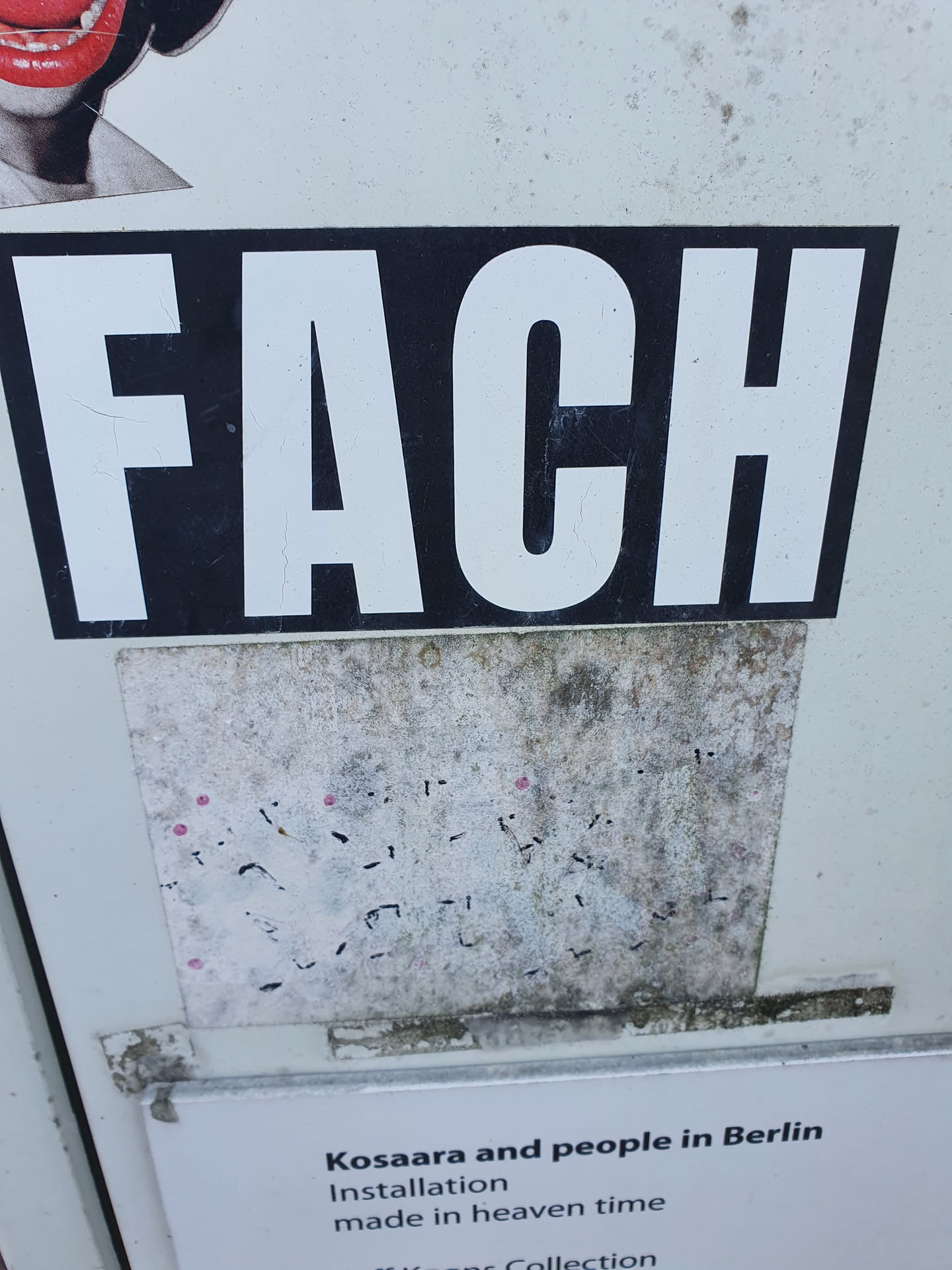A black and white sticker with the word "FACH" in bold, uppercase letters. Below it is a smaller, dirty sticker with illegible markings.  The larger sticker has a minimalist design.