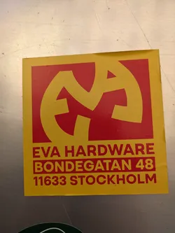 A yellow and red sticker with a logo and address information for Eva Hardware located at Bondegatan 48, 11633 Stockholm.