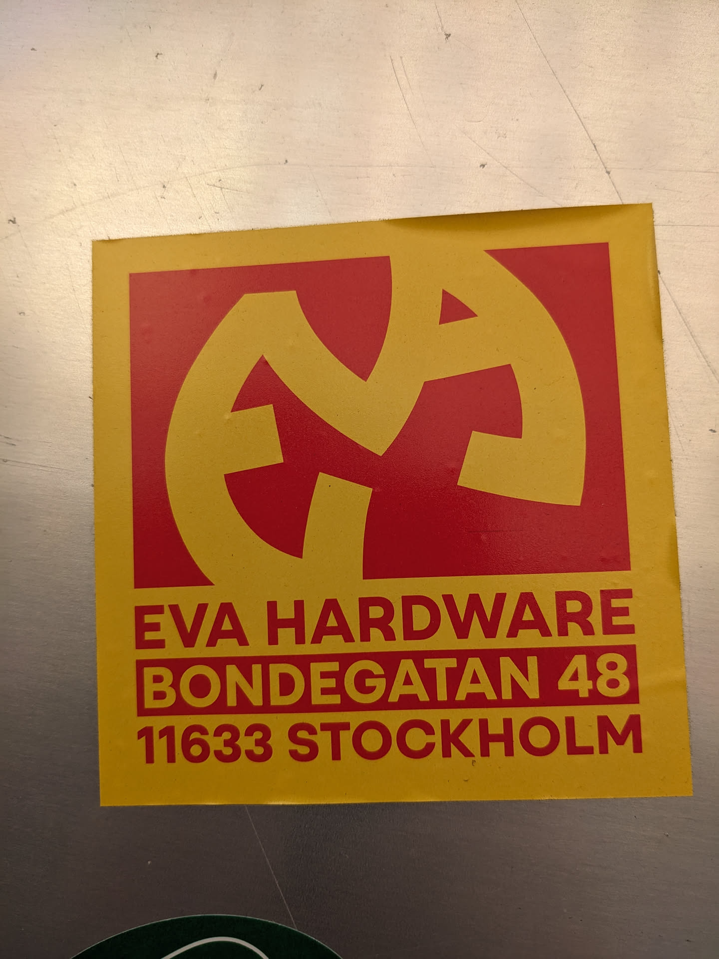A yellow and red sticker with a logo and address information for Eva Hardware located at Bondegatan 48, 11633 Stockholm.